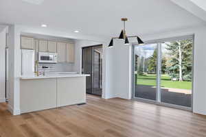 Kitchen featuring white appliances, light wood-style flooring, hanging light fixtures, and light stone countertops