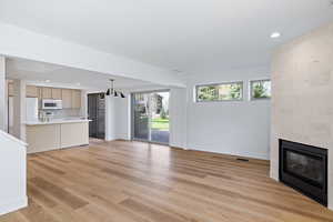 Unfurnished living room with a large fireplace, light wood-type flooring, and hanging lights