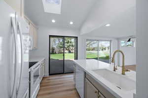 Kitchen with white appliances, lofted ceiling, light wood-style flooring, a skylight, and light stone counters