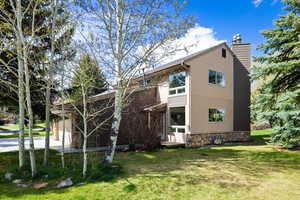 Back of property featuring a chimney, a yard, stone siding, and an attached garage