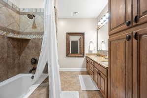 Full bath with double vanity, shower / tub combo with curtain, and light tile patterned floors