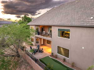 Back of house at dusk with a balcony, stucco siding, a patio area, and a putting green