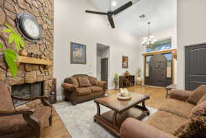 Living room featuring a chandelier, wood finished floors, a ceiling fan, a fireplace, and lofted ceiling