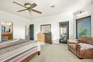 Bedroom with light carpet, ceiling fan, multiple windows, and ensuite bathroom