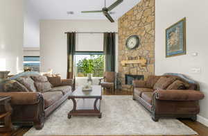 Living area featuring a stone fireplace, dark wood-style floors, and a ceiling fan