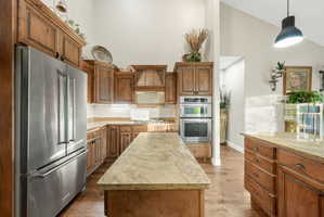 Kitchen featuring stainless steel appliances, wood finish cabinetry, vaulted ceiling, and decorative light fixtures