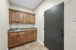 Bar area with wood finish cabinets, light tile patterned floors, and dark stone countertops
