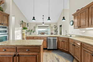 Kitchen featuring wood finish cabinets, a peninsula, stainless steel appliances, light stone countertops, and lofted ceiling