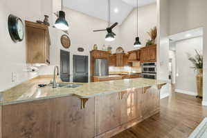 Kitchen featuring wood finish cabinetry, a peninsula, dark wood-style floors, vaulted ceiling, and stainless steel appliances