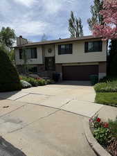 Raised ranch with brick siding, driveway, an attached garage, and a chimney