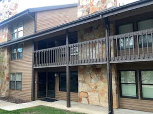 Rear view of house with stone siding, a chimney, a balcony, a yard, and a patio