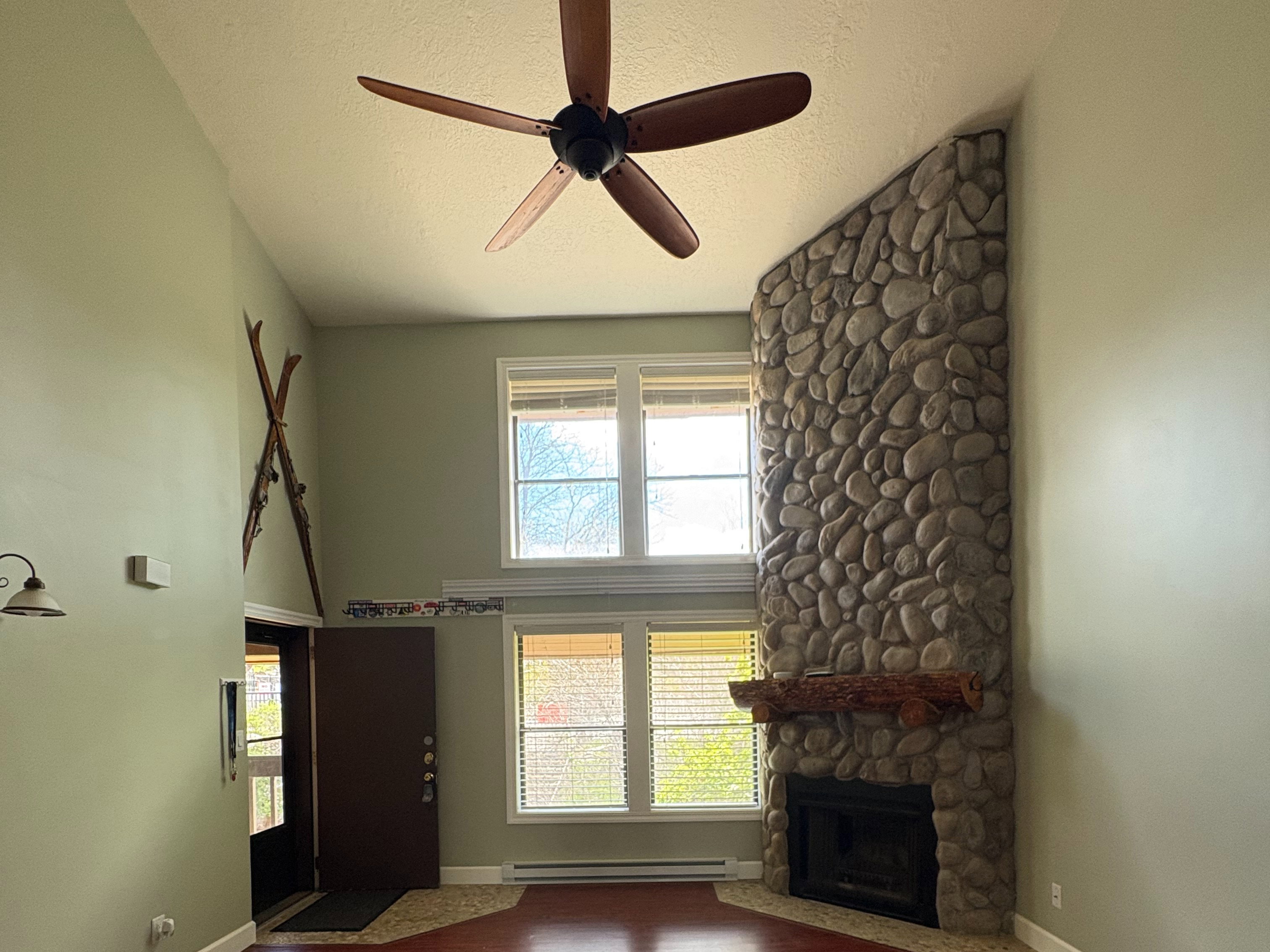 Living area featuring a floor-to-ceiling stone fireplace with a wood mantle, wood-finish flooring, and a vaulted ceiling with a ceiling fan