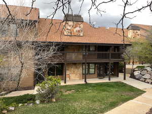 Rear view of house with stone siding, a yard, a shingled roof, and a balcony
