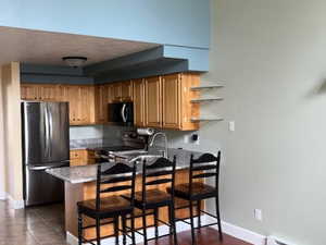 Kitchen with wood finish cabinets, a kitchen bar, stainless steel appliances, a baseboard heating unit, and a peninsula