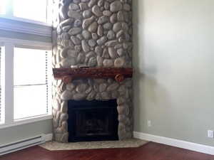 Unfurnished living room featuring a baseboard heating unit, dark wood-style flooring, and a stone fireplace