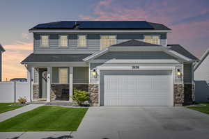 View of front of home featuring an attached garage, stone siding, concrete driveway, roof mounted solar panels, and covered porch