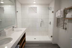 Full bathroom with double vanity, a towel warmer, a stall shower, dark wood-type flooring, and radiator