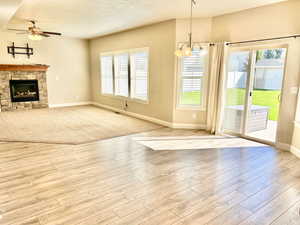 Unfurnished living room featuring plenty of natural light, ceiling fan, a stone fireplace, and hanging lights
