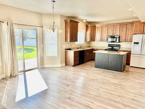 Kitchen featuring black appliances, a center island, suspended lighting, light wood finished floors, and light stone countertops