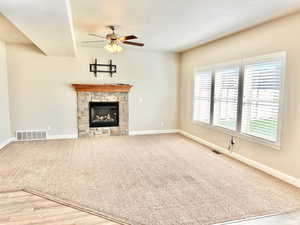 Unfurnished living room featuring ceiling fan, a fireplace, light carpet, and light wood-style floors