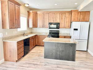 Kitchen with black appliances, light stone counters, a center island, light wood finished floors, and recessed lighting