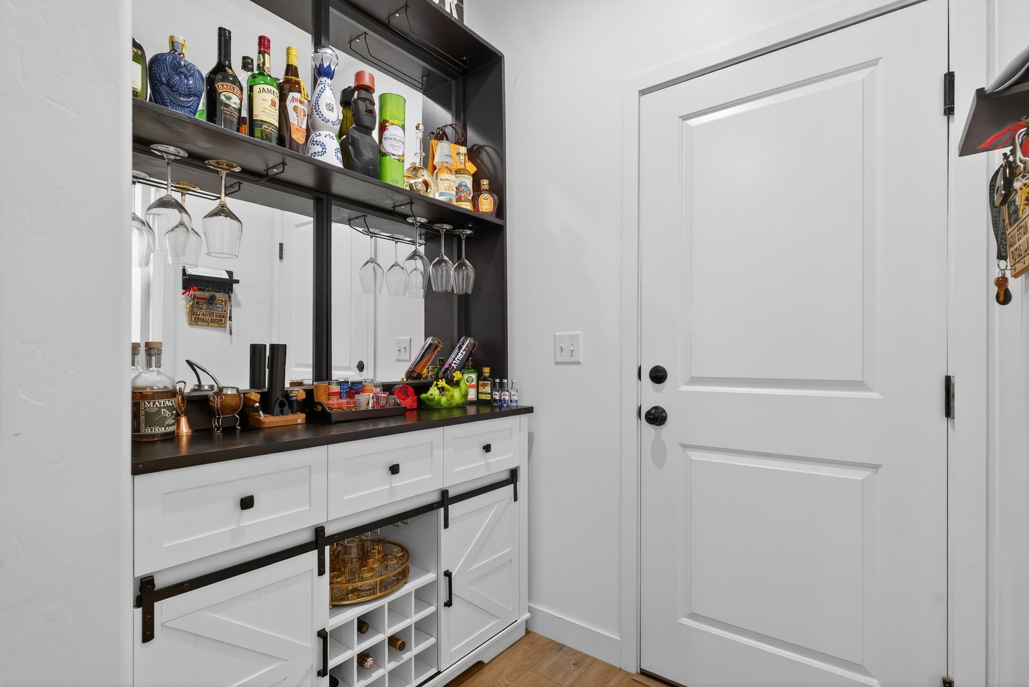 Indoor dry bar with open shelves, light wood-type flooring, and white cabinets