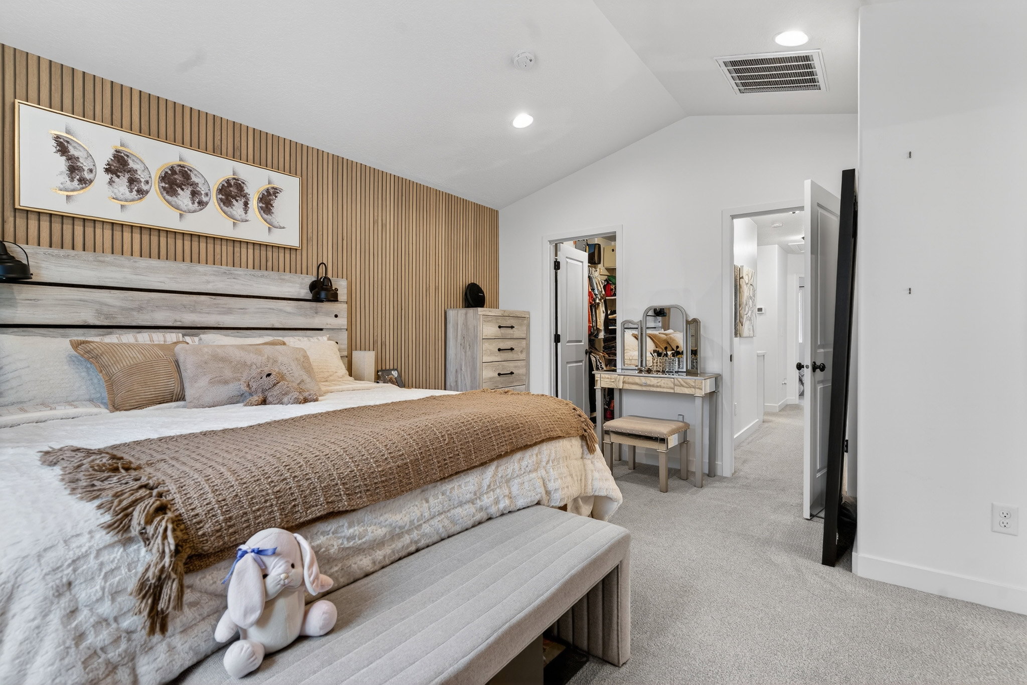 Bedroom with wooden walls, light carpet, a walk in closet, and an accent wall
