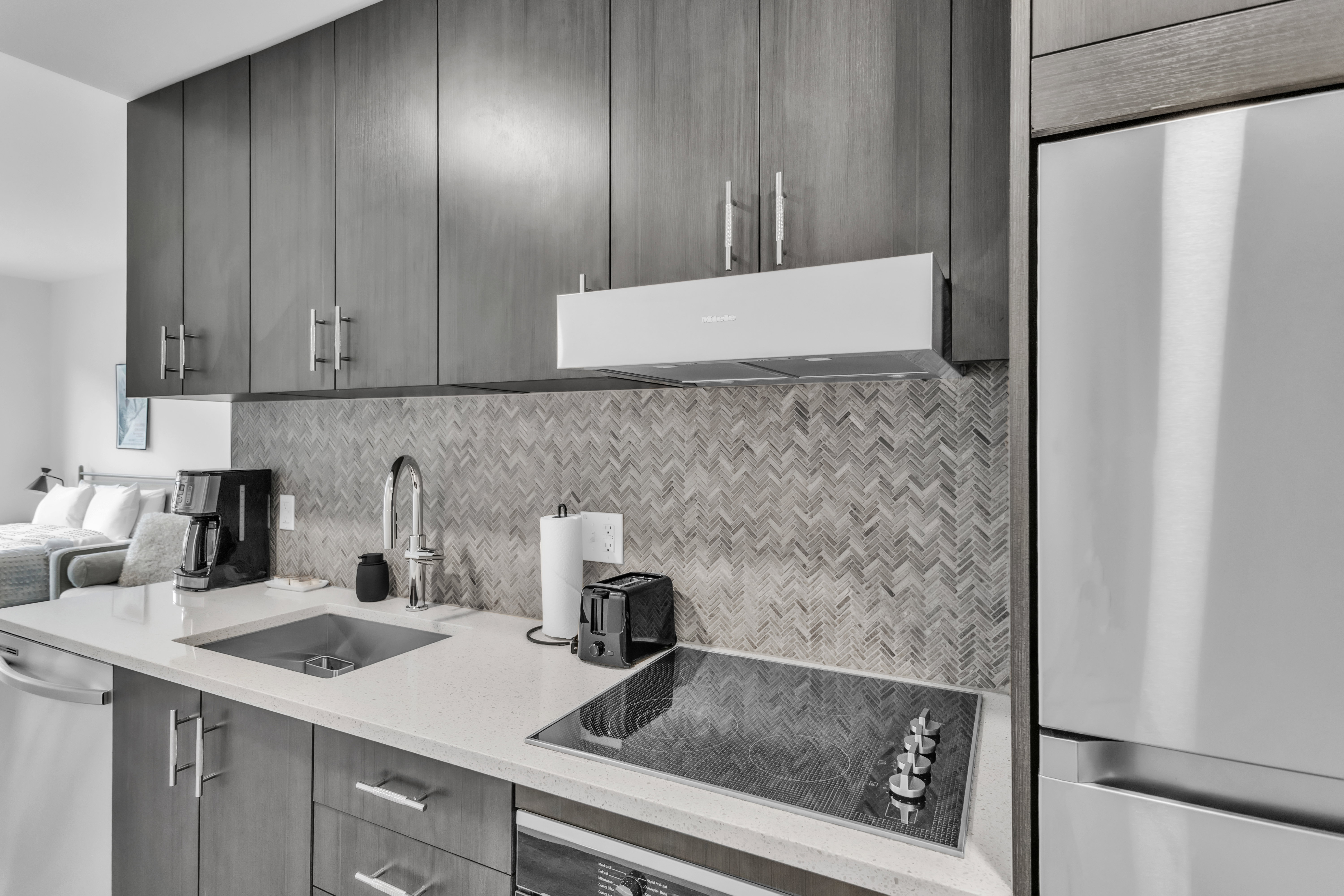 Kitchen with stainless steel appliances, light stone countertops, decorative backsplash, modern cabinets, and extractor fan