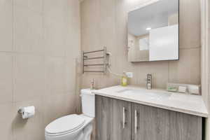 Bathroom featuring tile walls, vanity, radiator heating unit, and recessed lighting