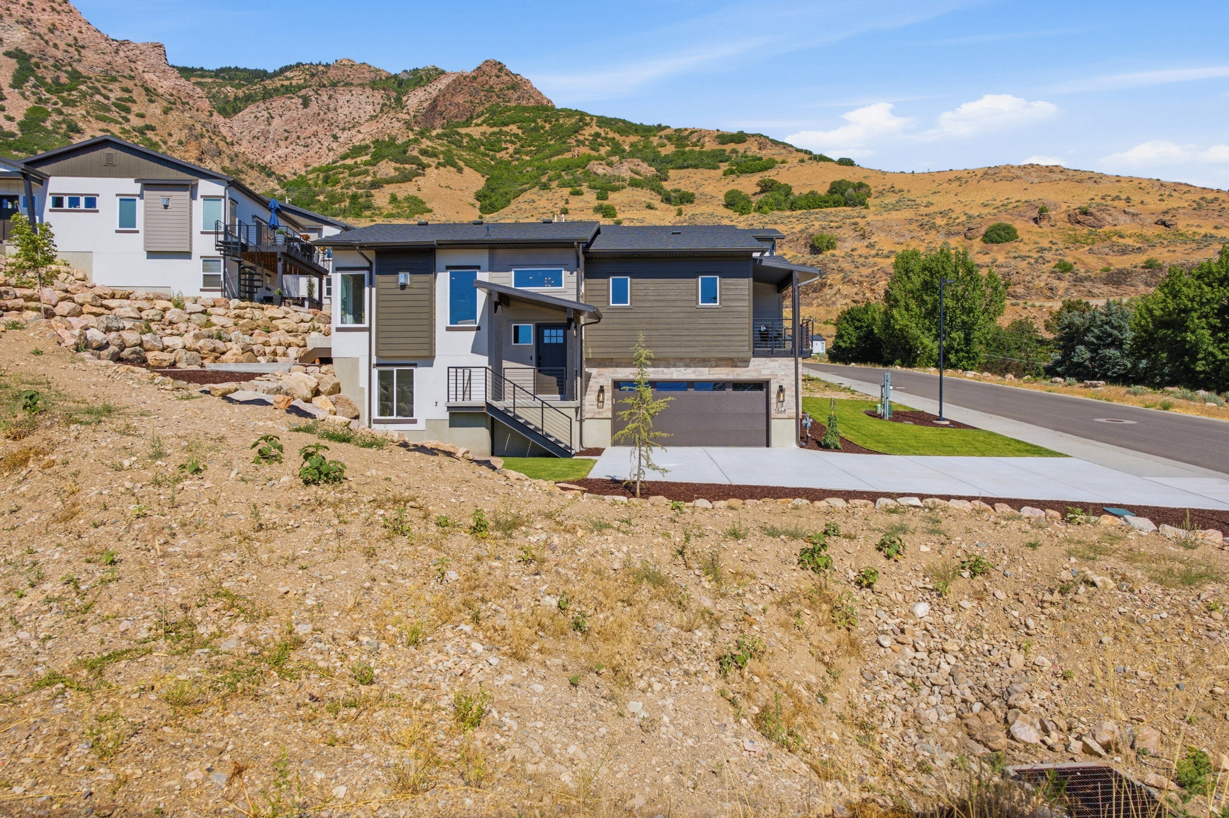 Contemporary multi-level exterior with a two-tone facade, attached garage, concrete driveway, and tiered landscaping