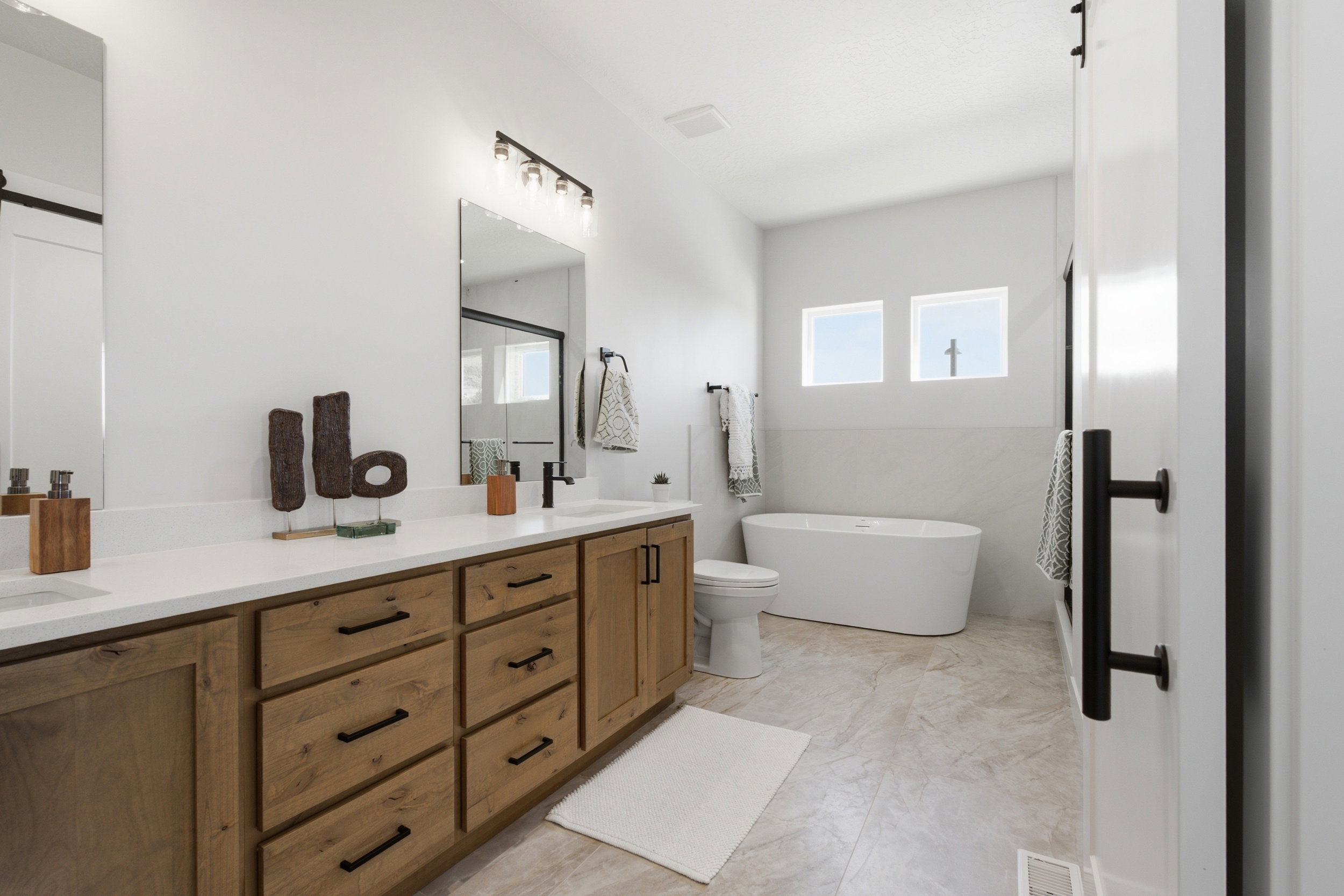 Bathroom featuring a dual vanity with wood-finish cabinetry, white countertops, and black hardware