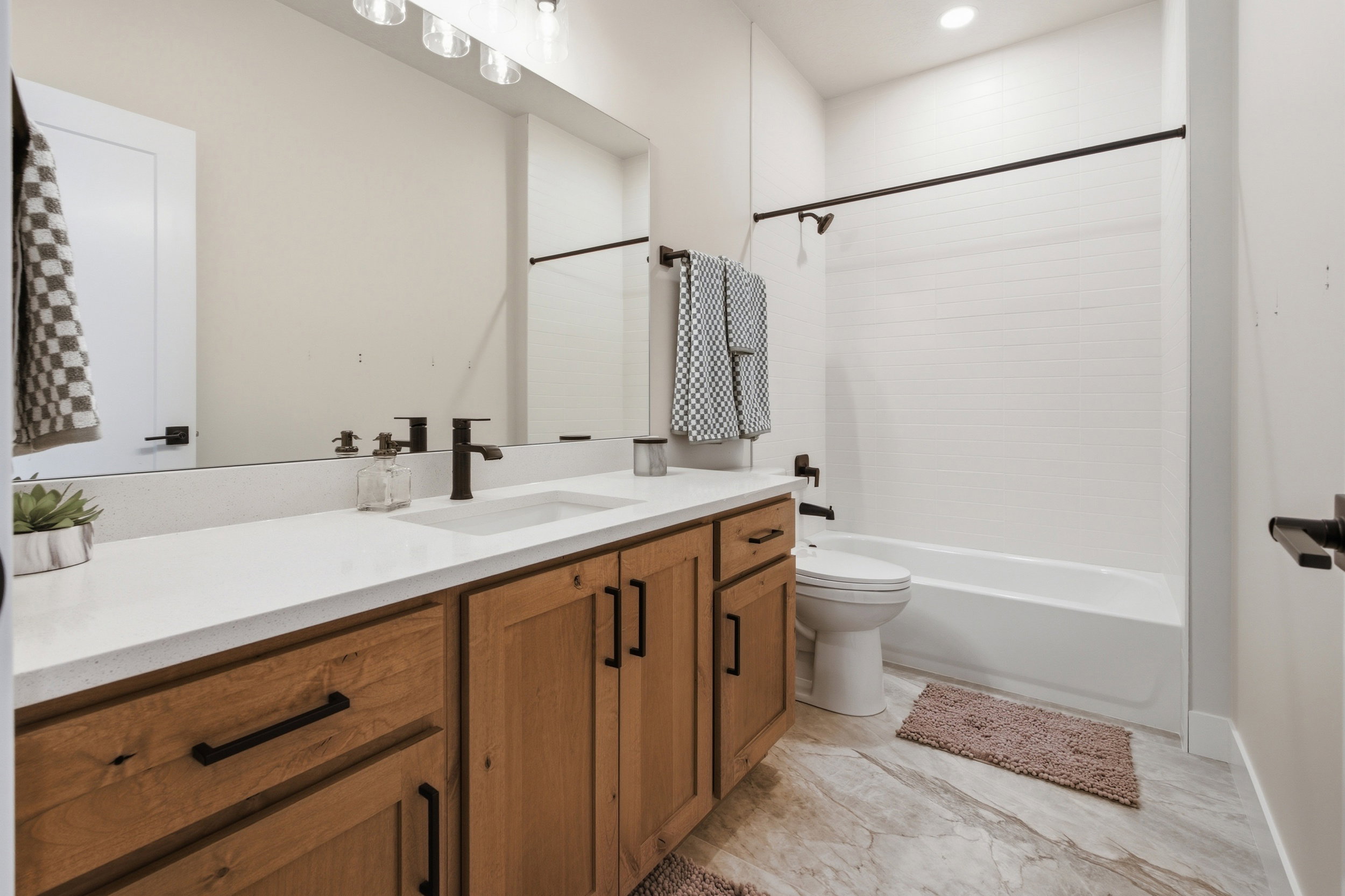 Contemporary bathroom featuring a light wood-finish double vanity with white countertops, matte black plumbing fixtures, and a large wall-mounted mirror