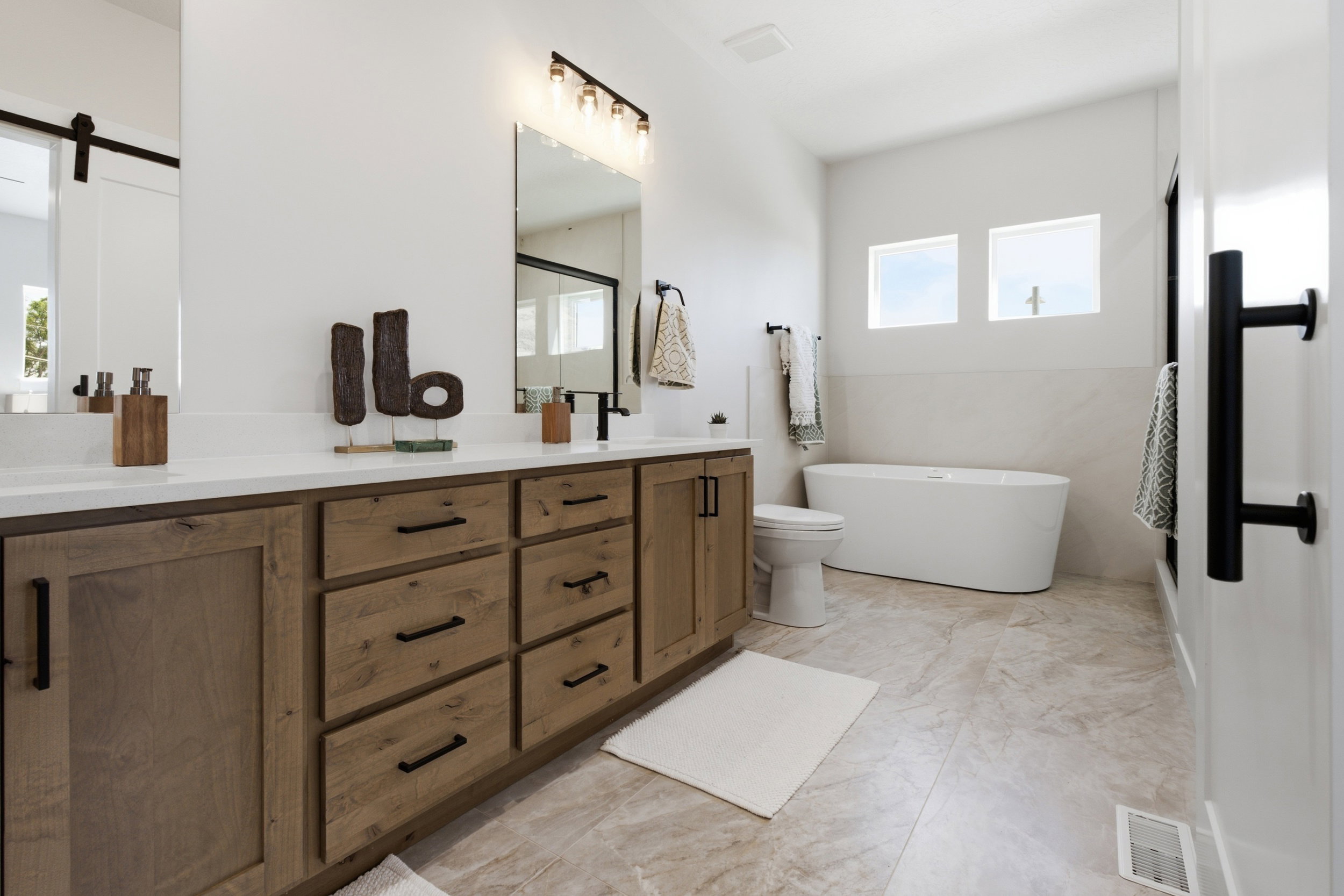Light-filled bathroom featuring a freestanding soaking tub, dual vanity with wood-finish cabinetry, and tiled flooring