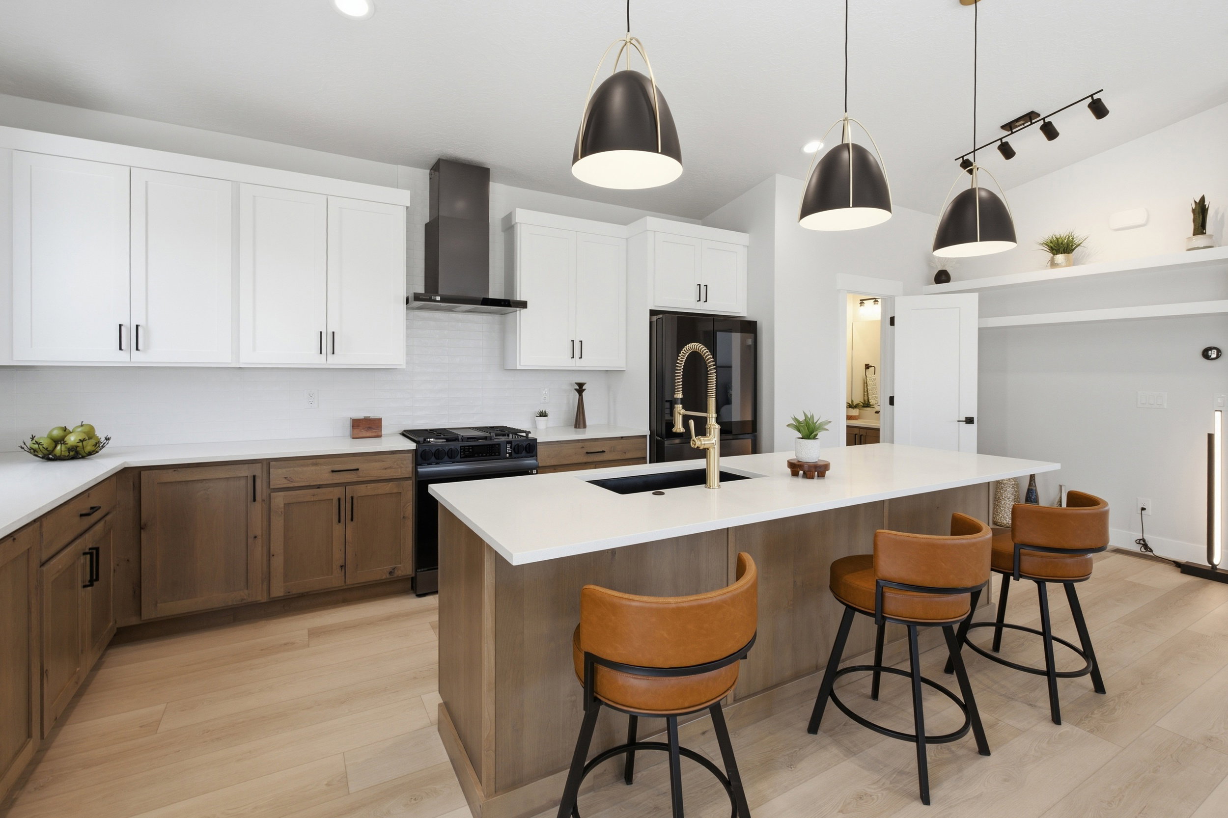 Kitchen featuring light wood-finish flooring, white upper cabinetry, natural wood-finish lower cabinetry, white subway tile backsplash, and a central island with a white countertop and gold-toned faucet