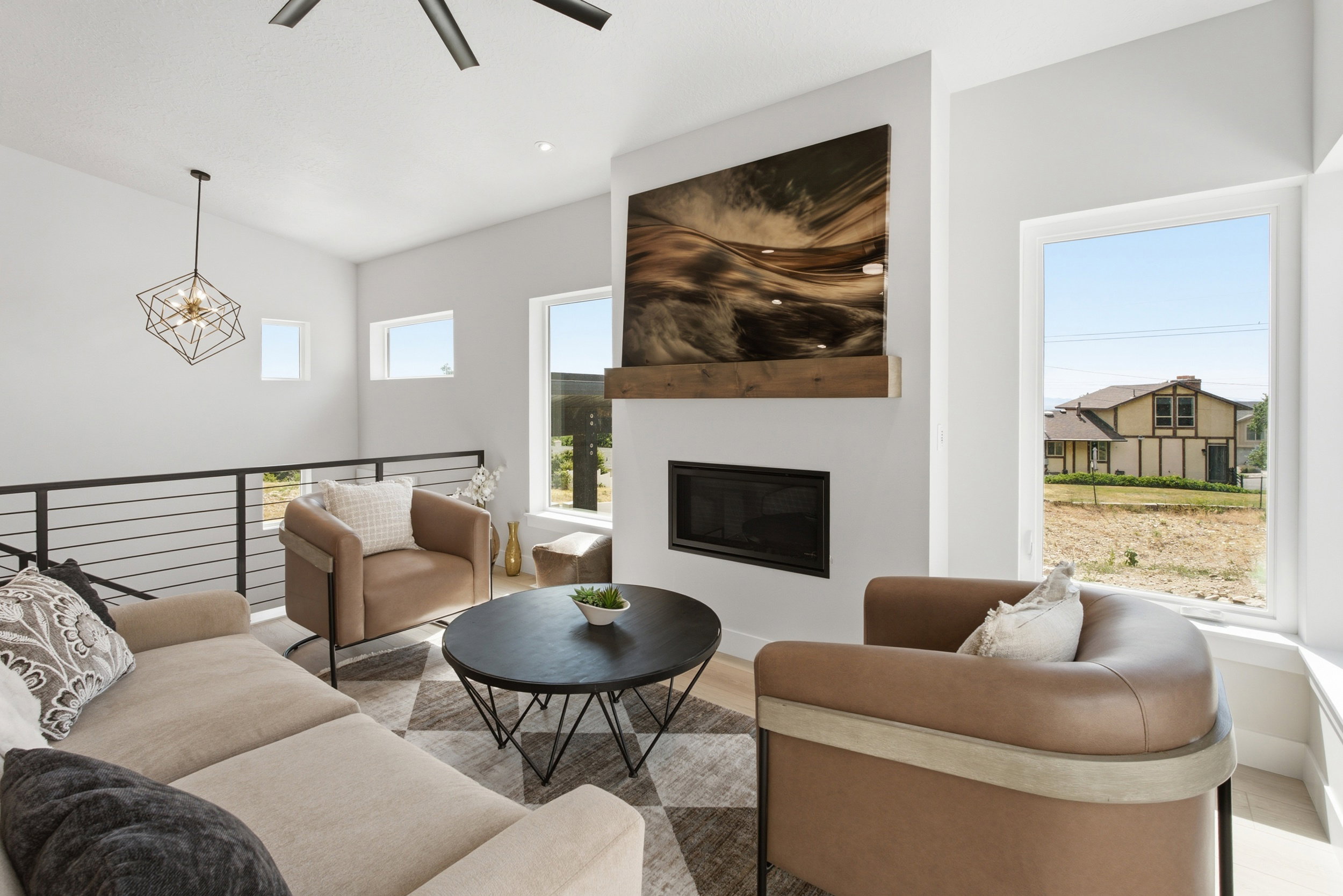 Living area featuring a floor-to-ceiling fireplace with a wood-finish mantel, multiple large windows, and a black metal railing overlooking a lower level