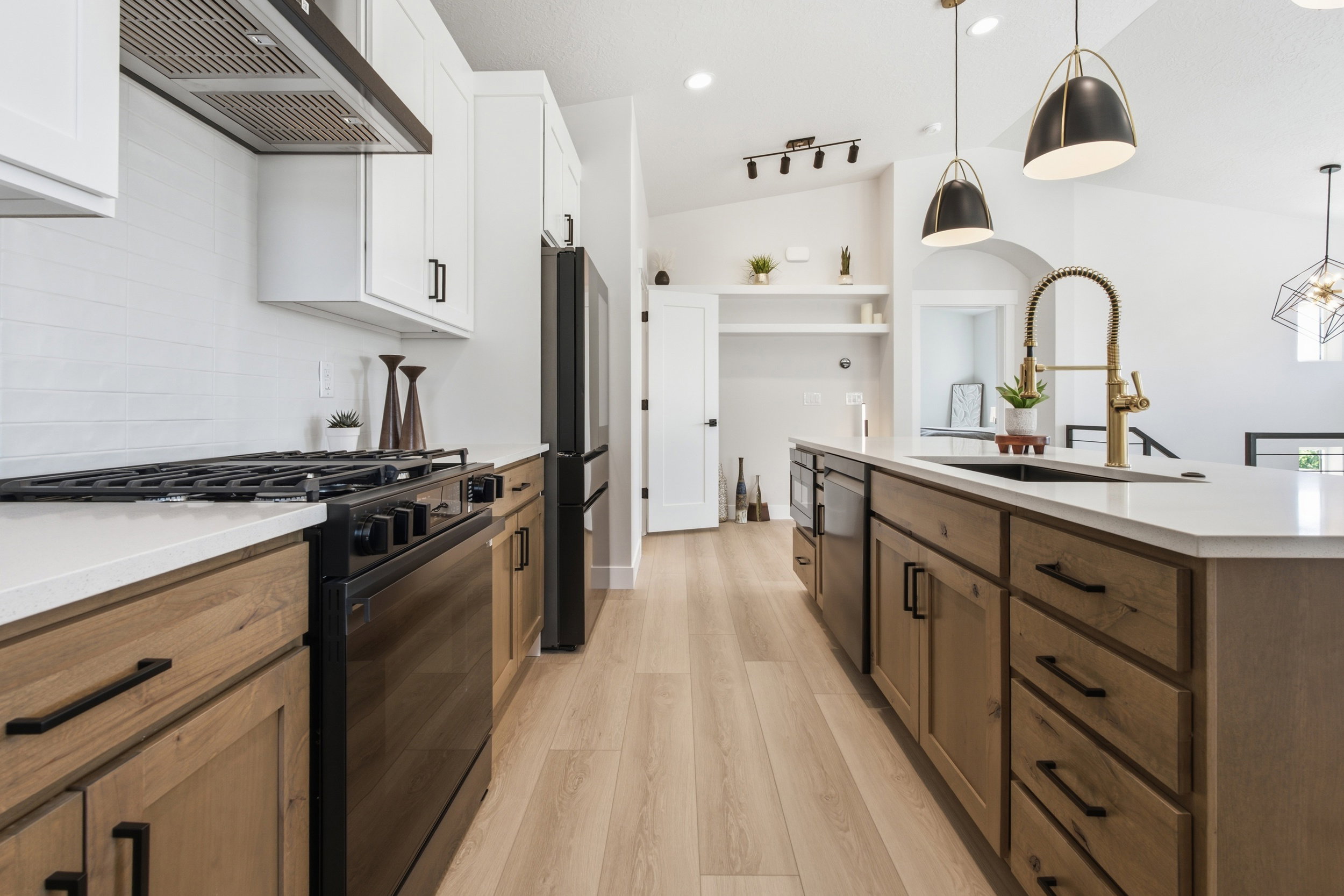 Open-concept kitchen featuring two-tone cabinetry, a central island with an integrated sink, black stainless steel appliances, and wood-finish flooring