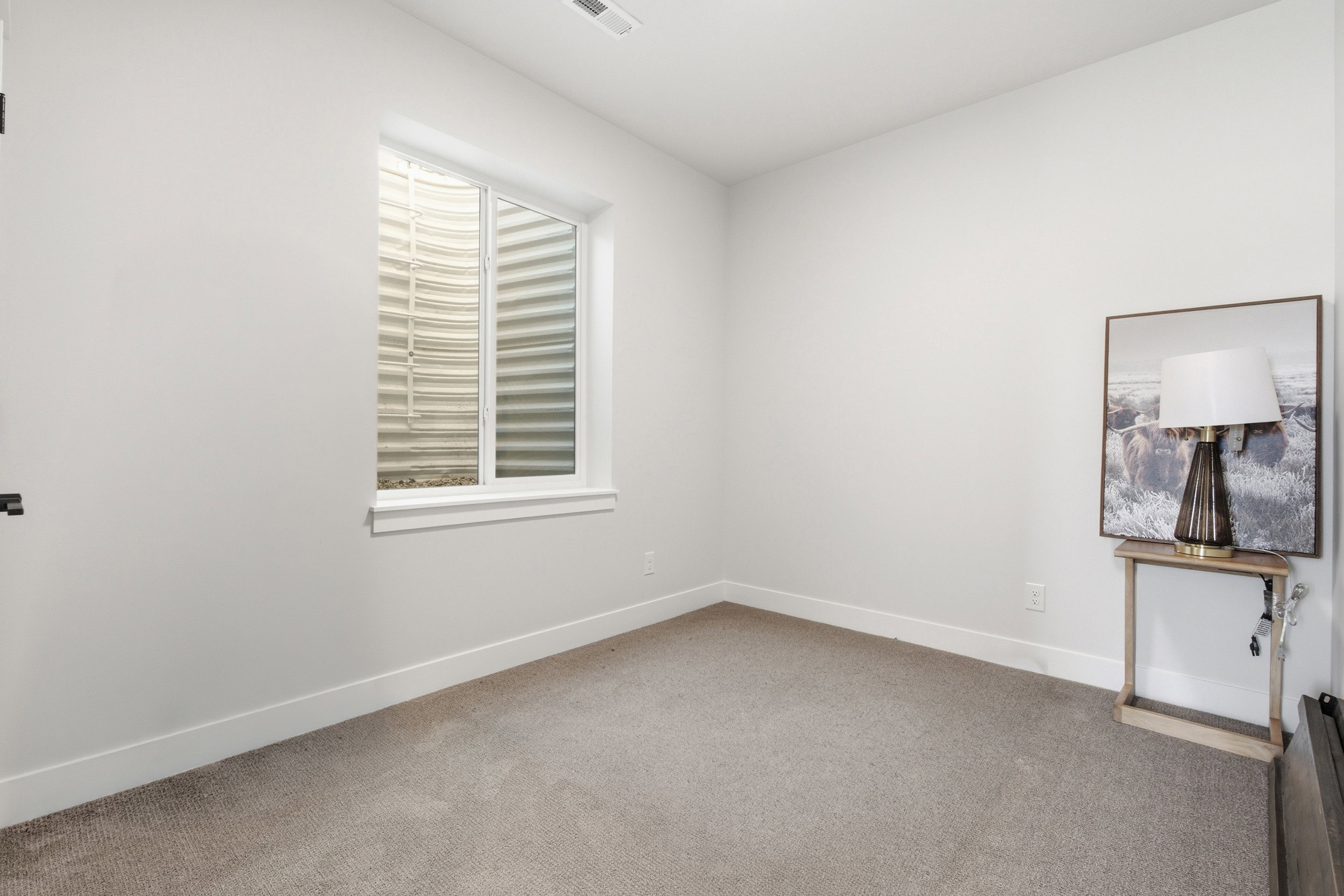 Room featuring a window with a window well, light-colored walls, and neutral carpet flooring