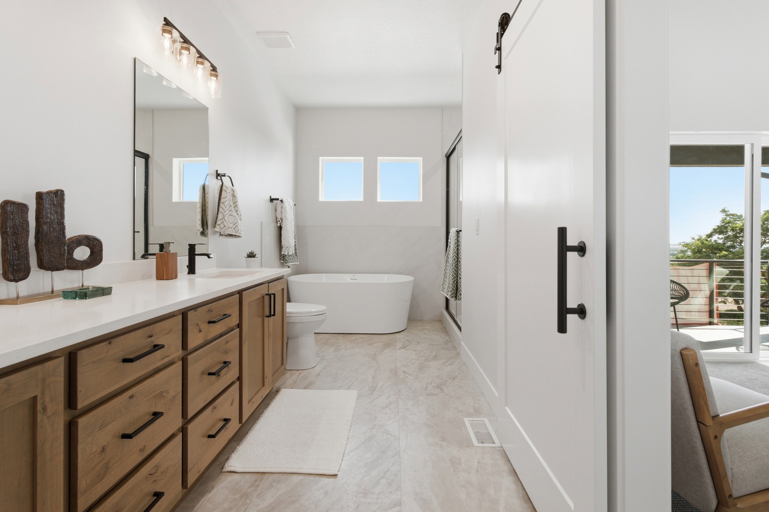 Contemporary bathroom featuring a double vanity with light wood-finish cabinetry, white countertops, and matte black fixtures