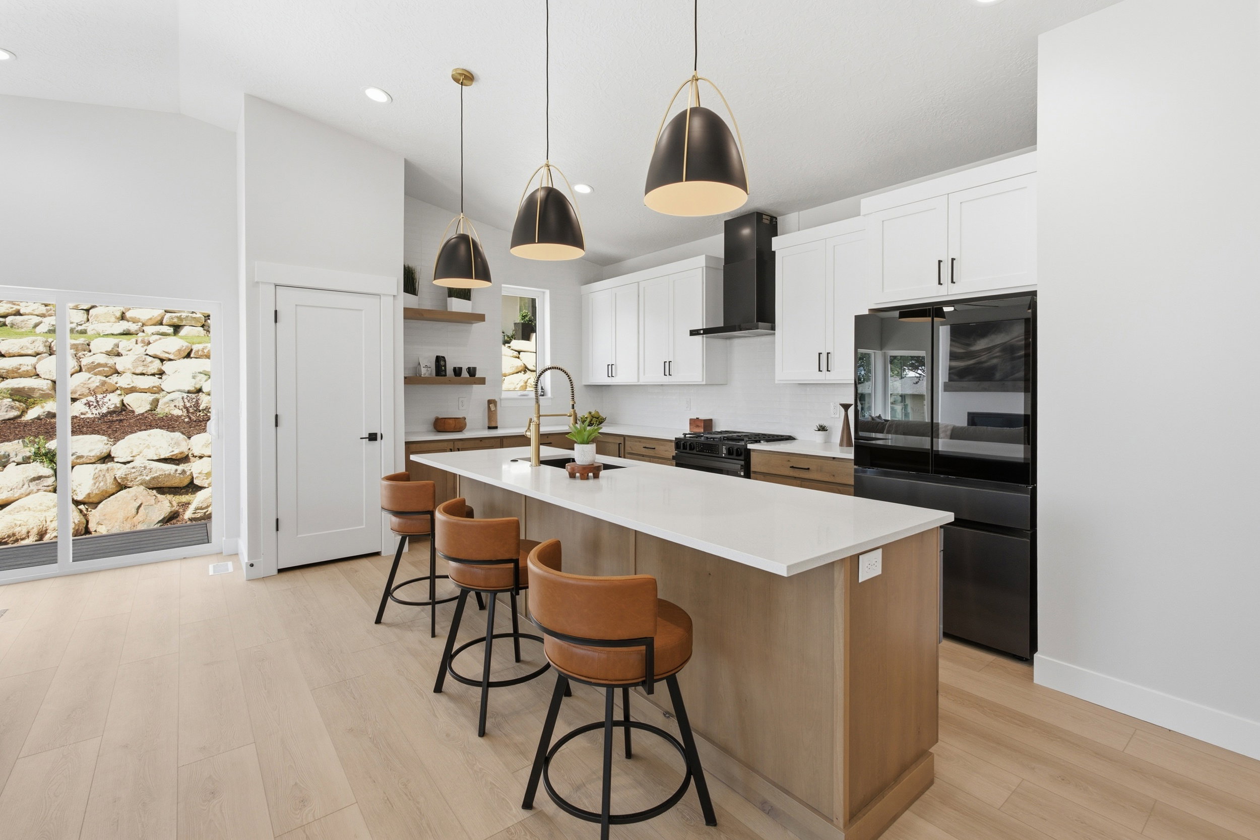 Contemporary kitchen featuring a large island with a light-toned countertop, white upper cabinetry, natural wood-finish base cabinetry, and black appliances