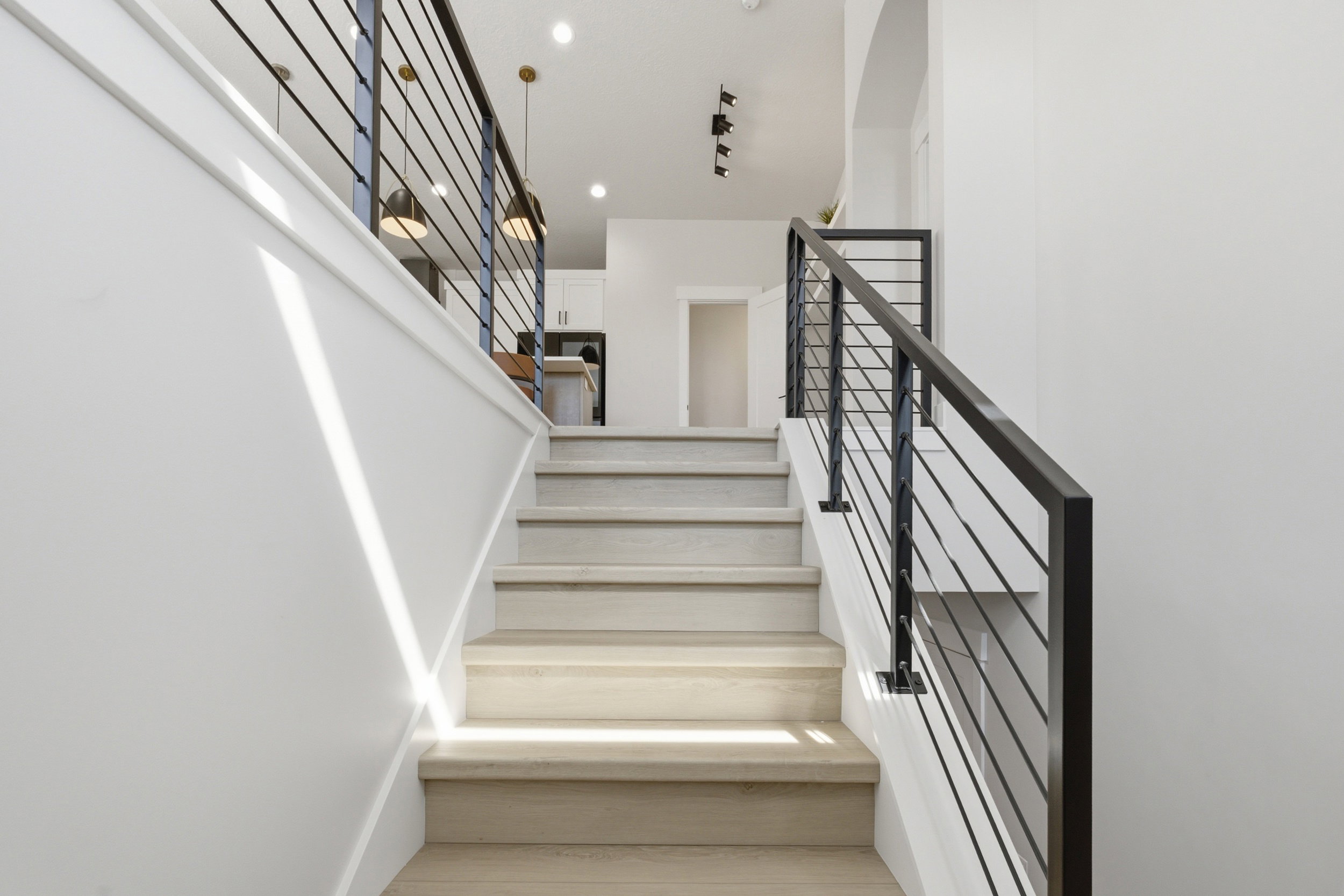 Modern staircase featuring light wood-finish treads and risers, black metal balusters, and white painted walls