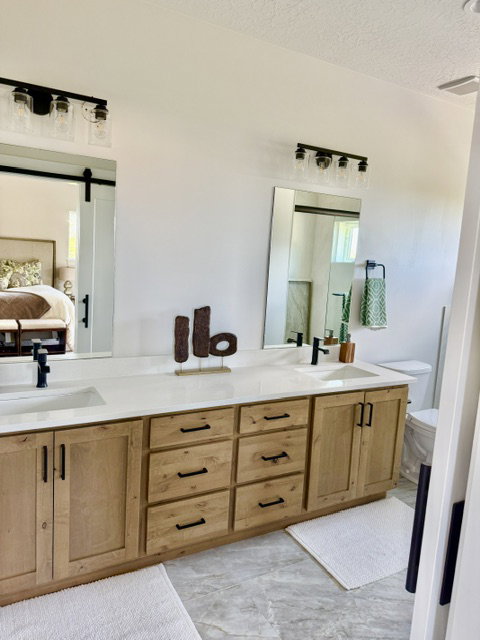 Double vanity featuring light wood cabinetry with black hardware, white countertops, and dual undermount sinks