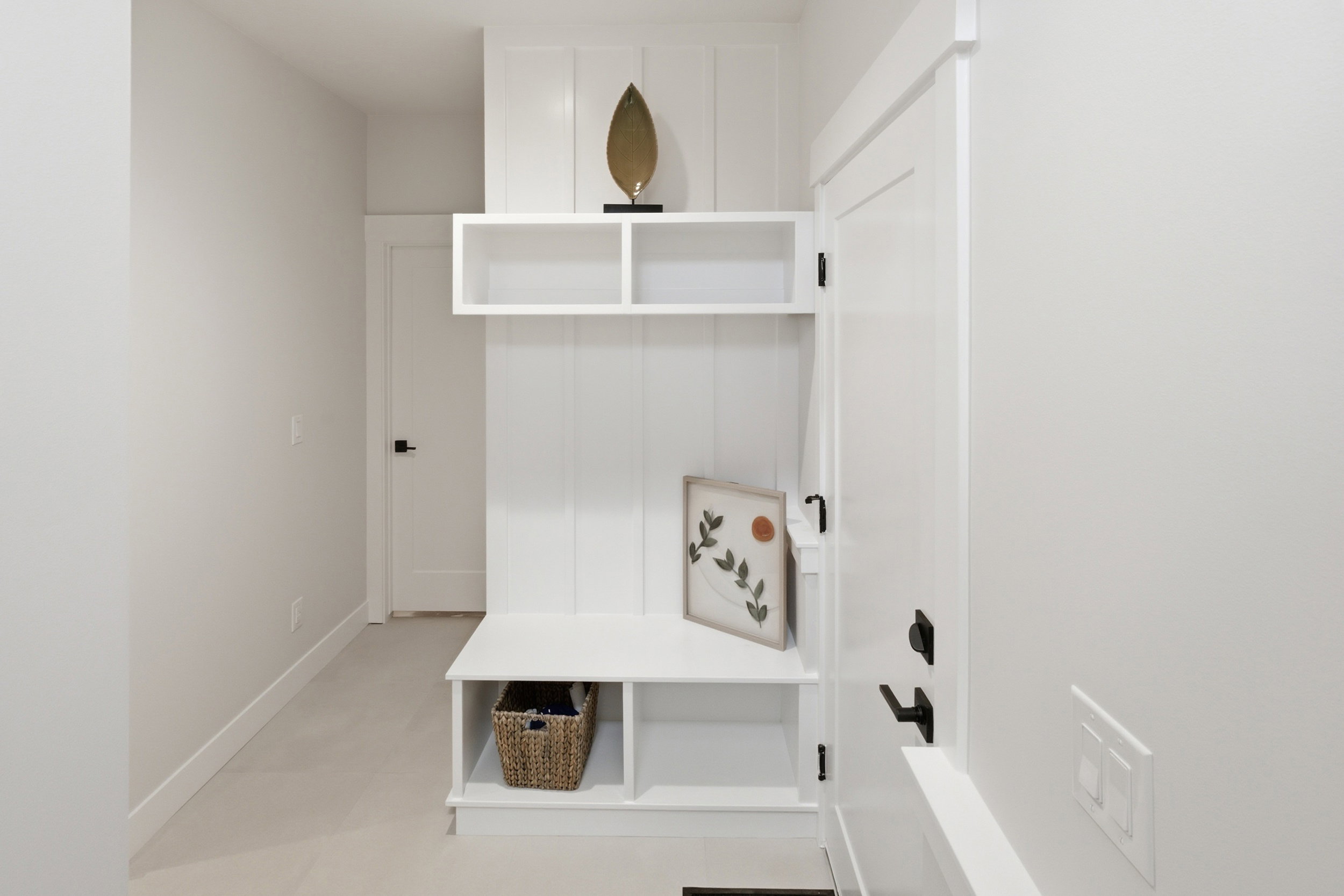 Built-in mudroom bench with cubby storage, upper shelving, and vertical paneling, complemented by a white interior door with matte black hardware