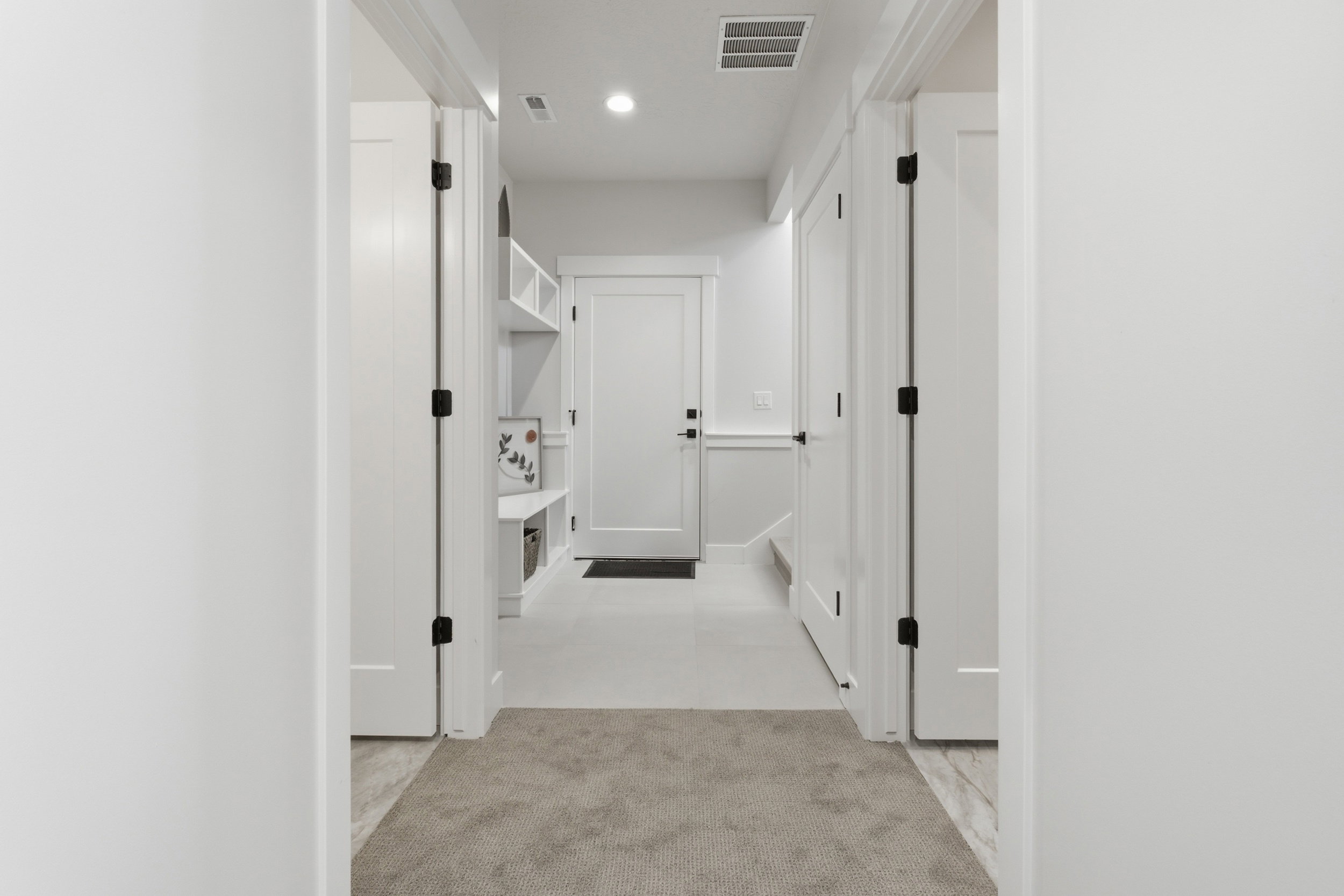 Hallway featuring light gray carpeting, white walls, and multiple white panel doors with matte black hardware