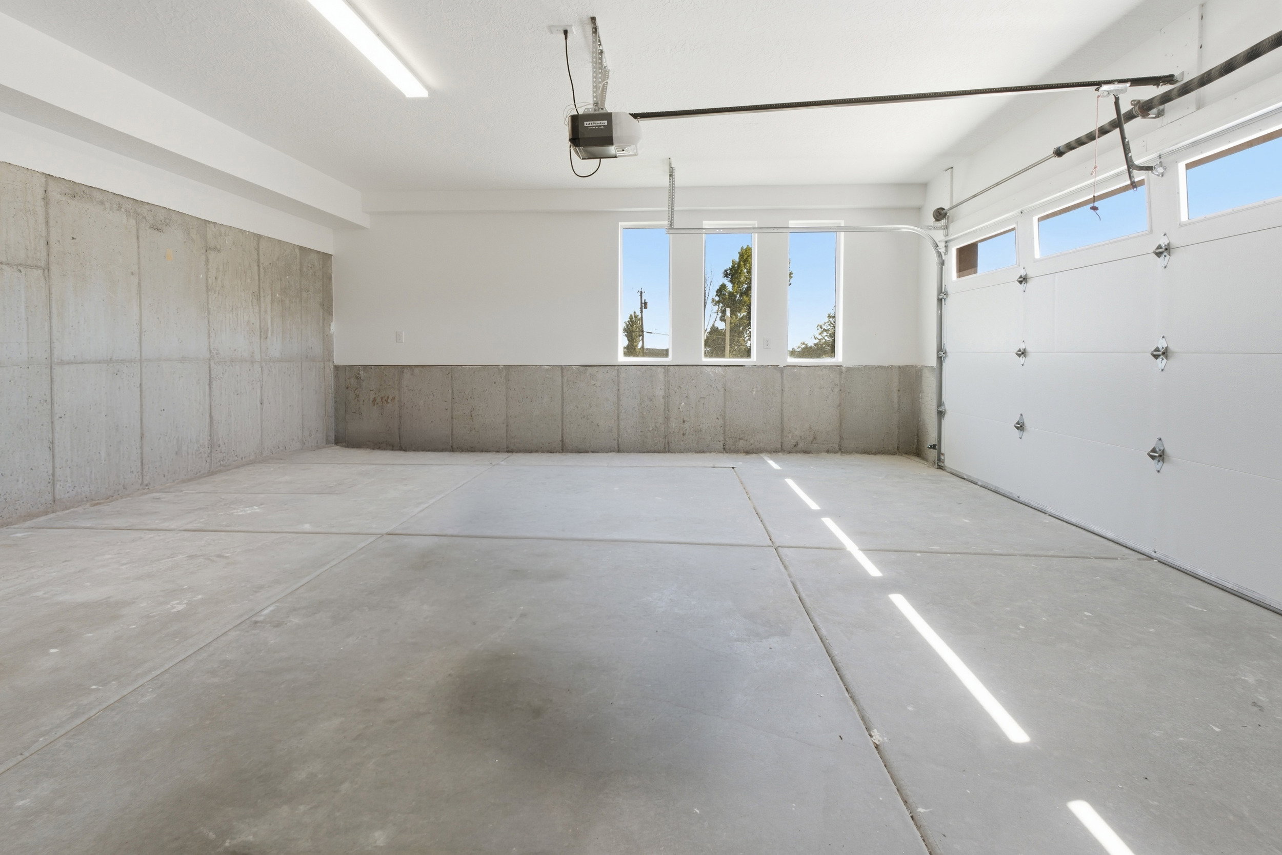 Spacious garage featuring a concrete floor, exposed concrete lower walls, white painted upper walls, and fluorescent ceiling lighting