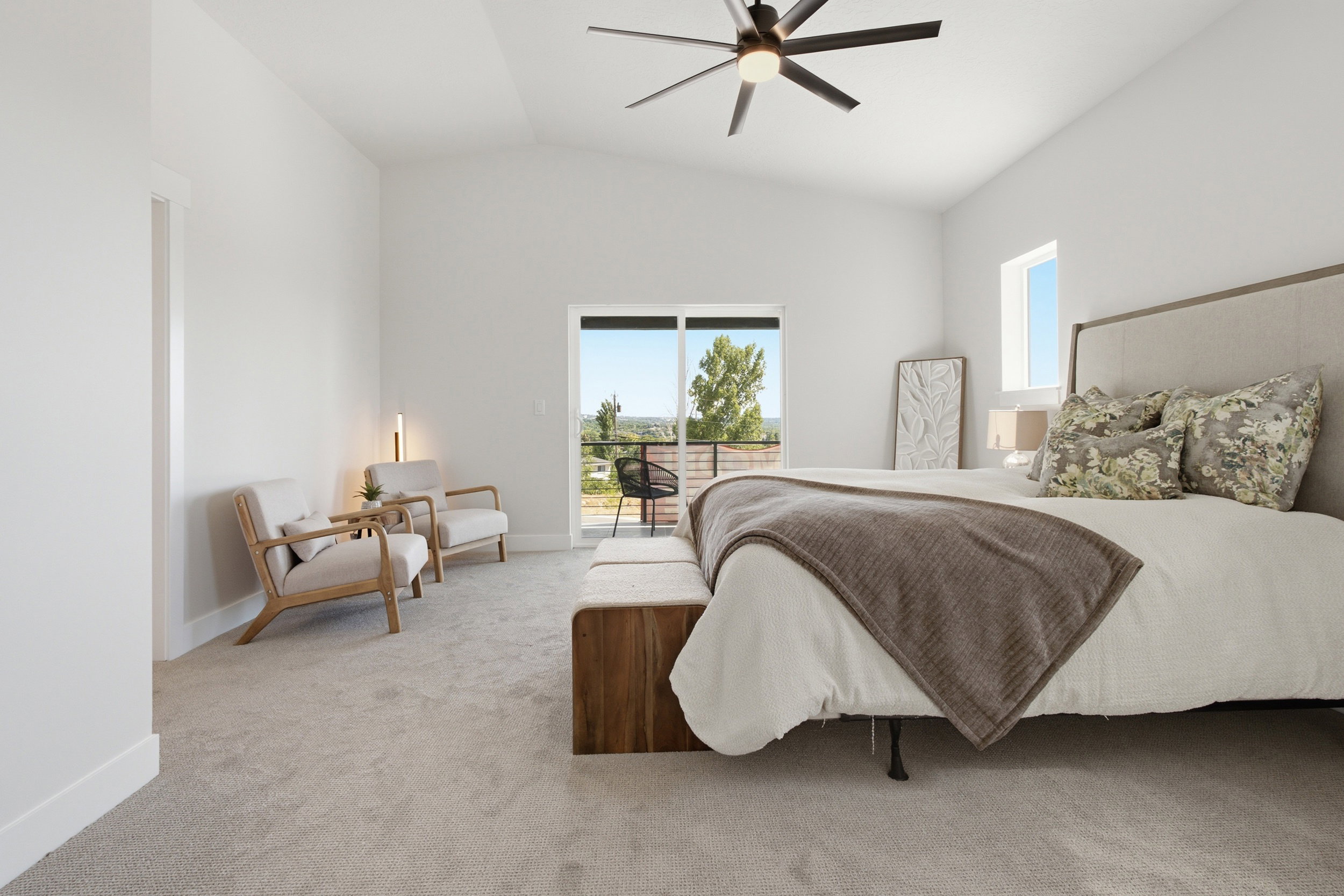 Spacious interior featuring a vaulted ceiling with a modern ceiling fan, light-colored carpeting, and a glass sliding door opening to an outdoor balcony