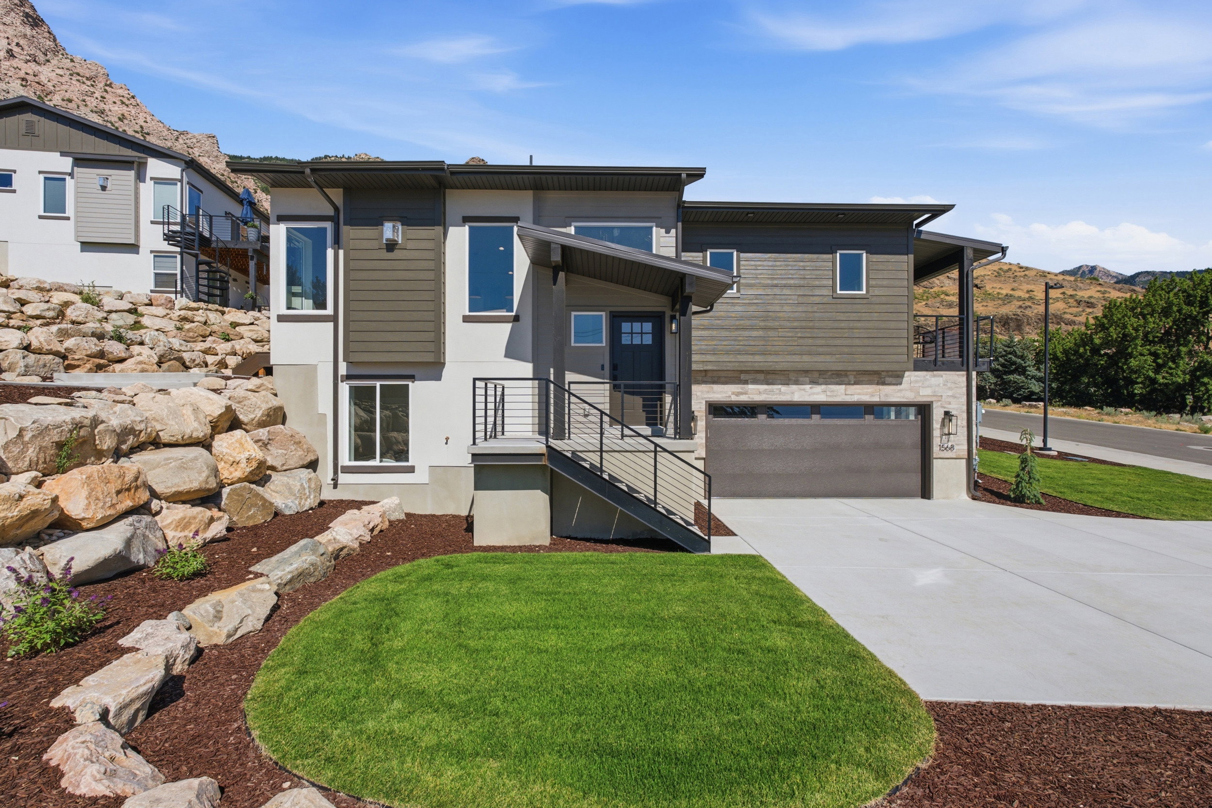 Contemporary two-story residence featuring a dark gray garage door, stacked stone accents, and a covered entryway with black metal railings