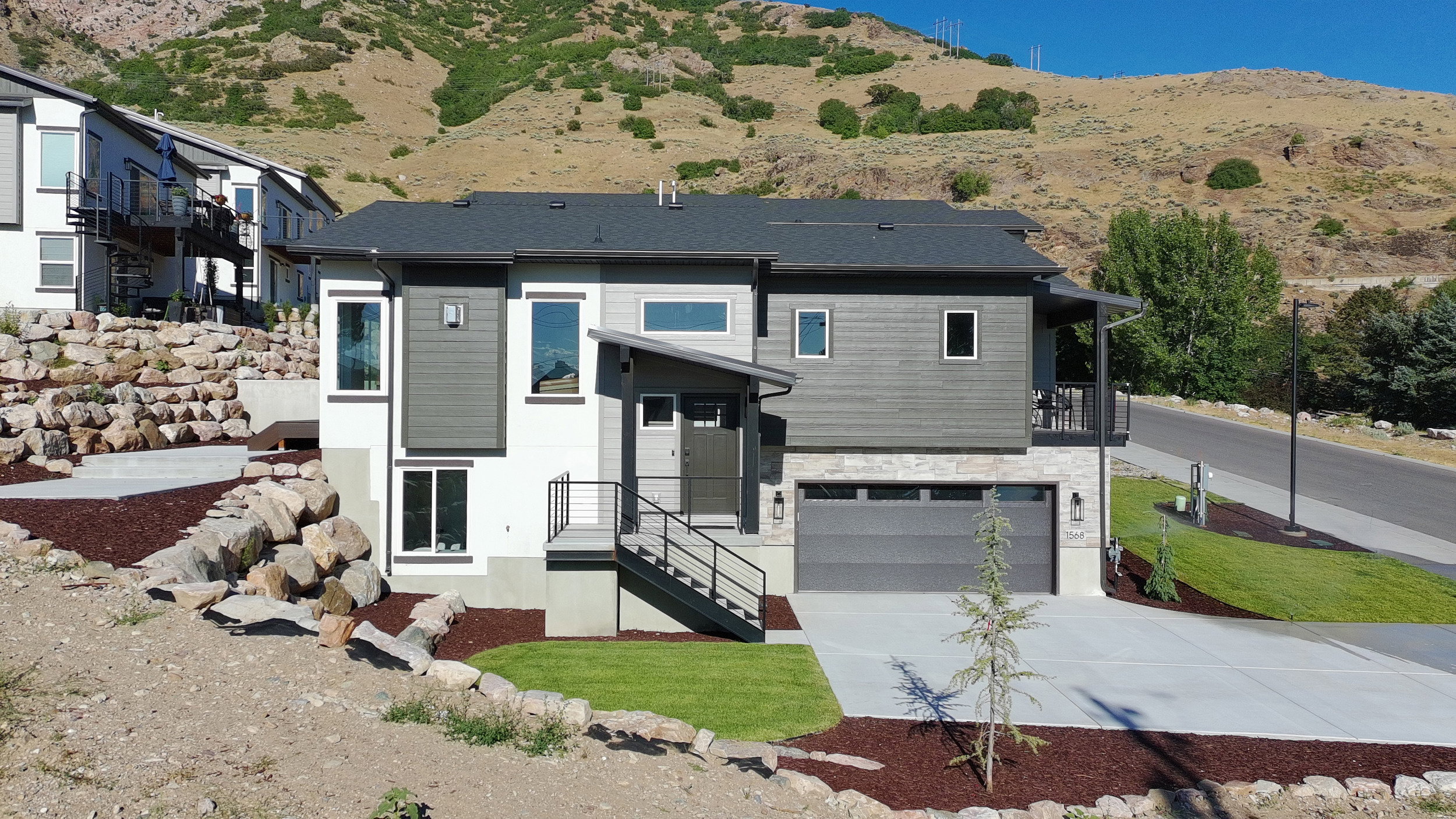 Contemporary exterior with mixed material facade, featuring a two-car garage, concrete driveway, and an elevated front entry with modern railings