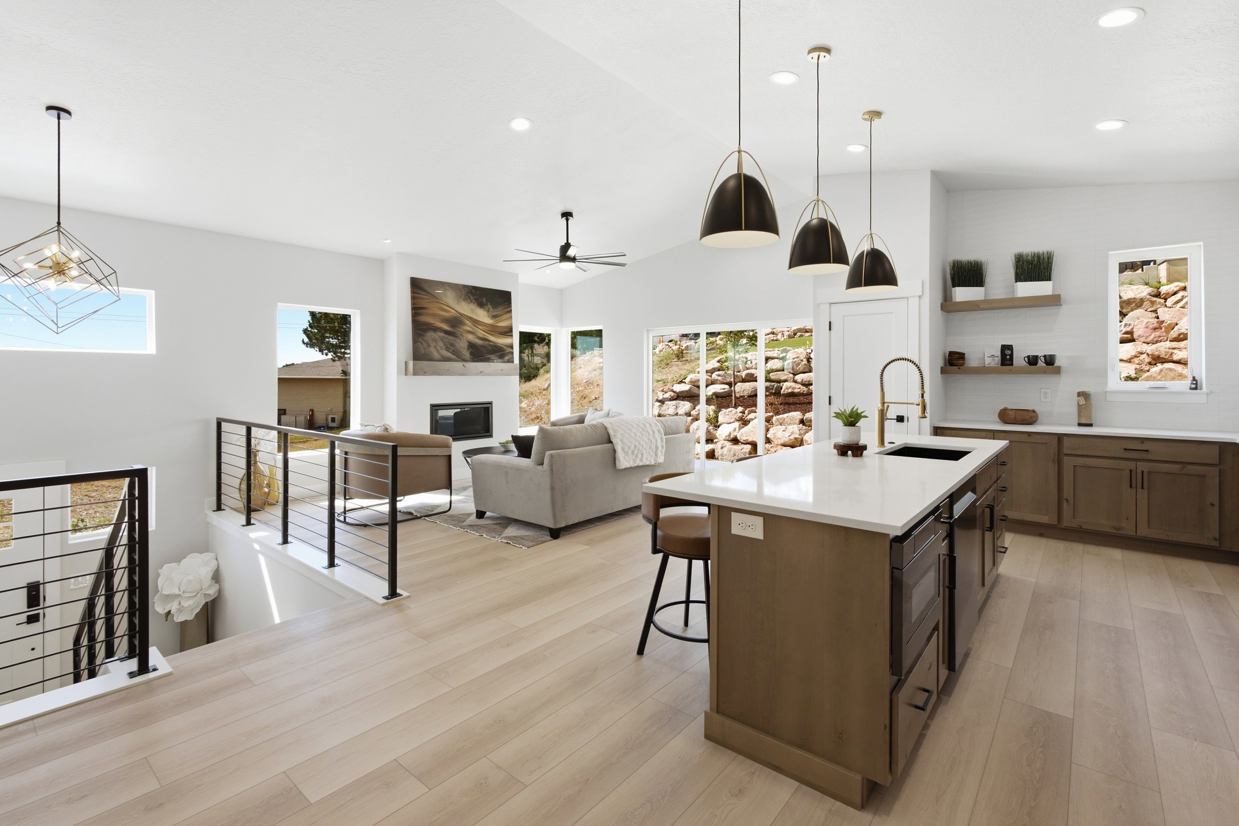 Open-concept living area featuring light wood-finish flooring, a modern kitchen island with an integrated sink and white countertop, and a living room with a fireplace and large windows