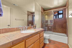 Bathroom featuring vanity, enclosed tub / shower combo, and dark tile patterned floors