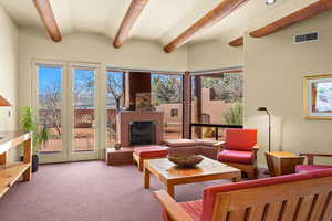 Living area with a fireplace with raised hearth, lofted ceiling with beams, and carpet